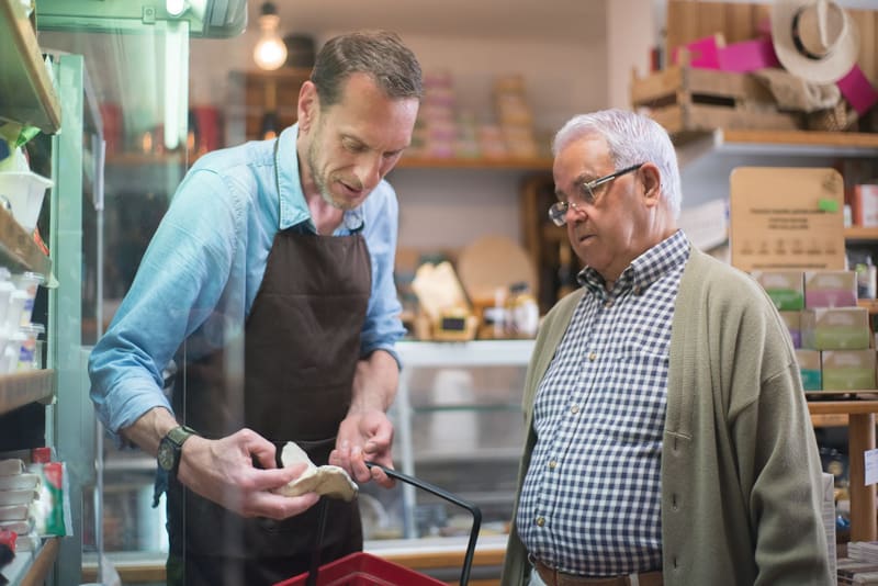 Tendero atendiendo a un cliente mayor en su tienda de barrio: así se empieza a conseguir clientes en un negocio local