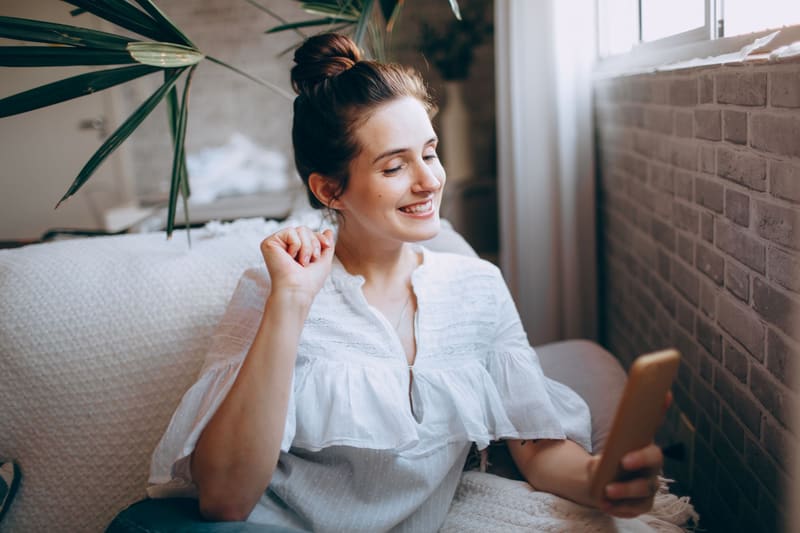 Clienta sonriendo en el sofá mientras lee en el móvil un correo de su negocio de confianza, el email marketing en acción