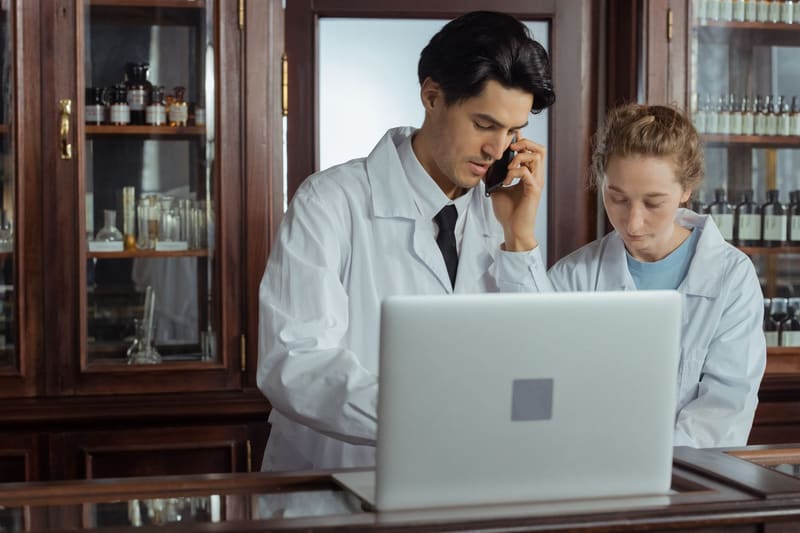 Farmacéutico llama por teléfono para resolver una incidencia de la web de su farmacia mientras revisa el portátil