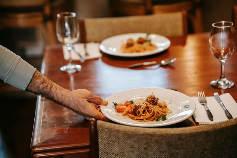 Camarero sirviendo un plato de pasta en la mesa de un restaurante que trabaja su marketing en Google