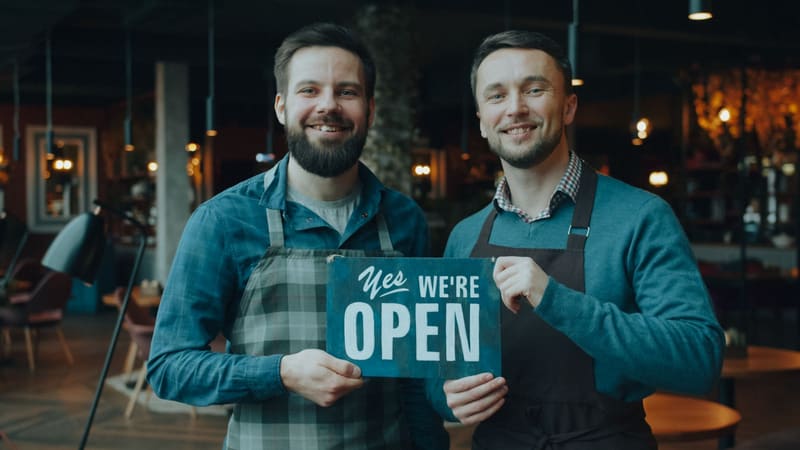 Dos socios de un restaurante junto al cartel de abierto